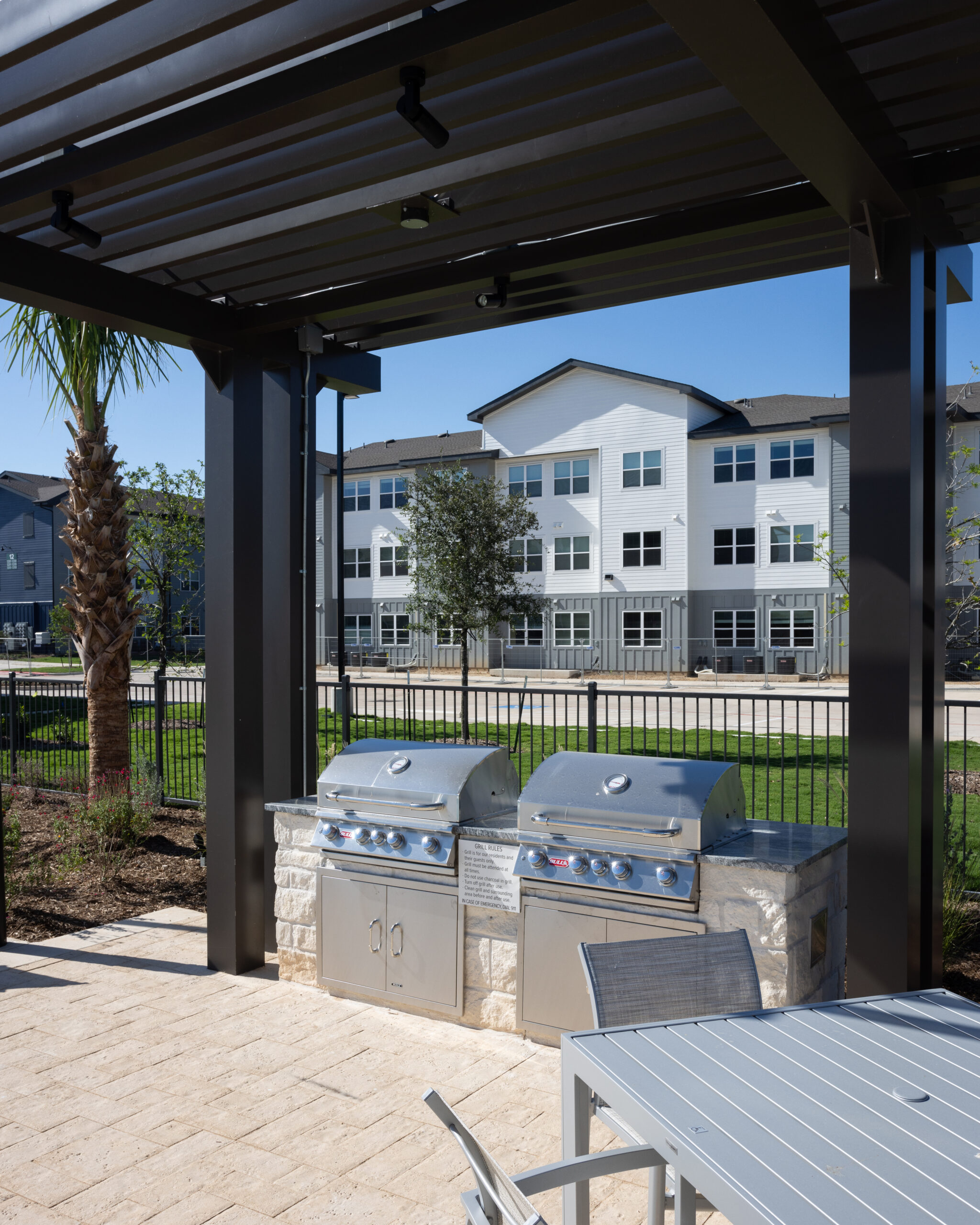 outdoor grill at sparking blue pool with lounge chairs and tables around it with building exteriors behind at prose evergreen in new braunfels, tx