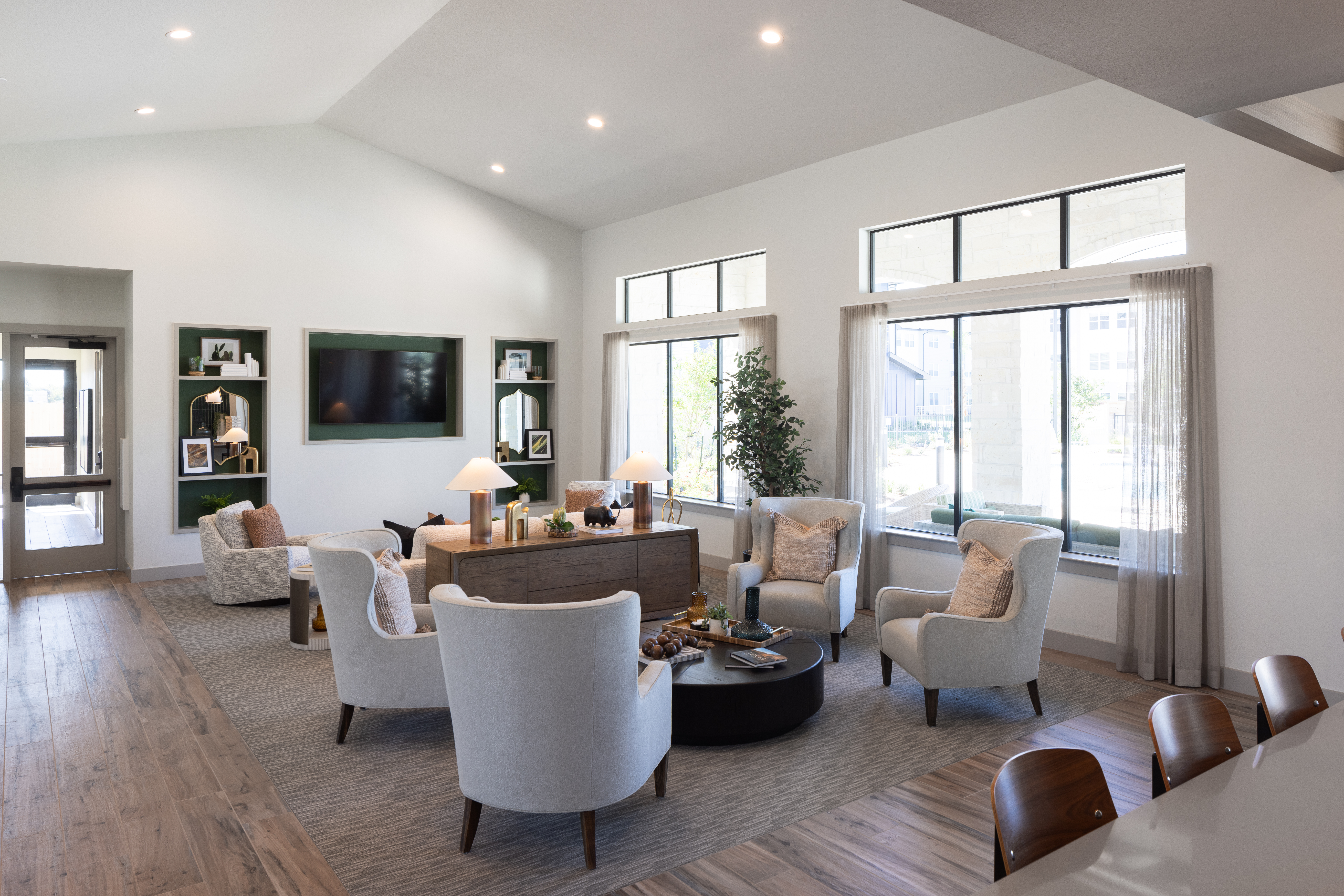 clubhouse area with ample soft seating, a tv in the back ground on a wall, with two large windows shining bright in the background at prose evergreen apartments in new braunfels, texas