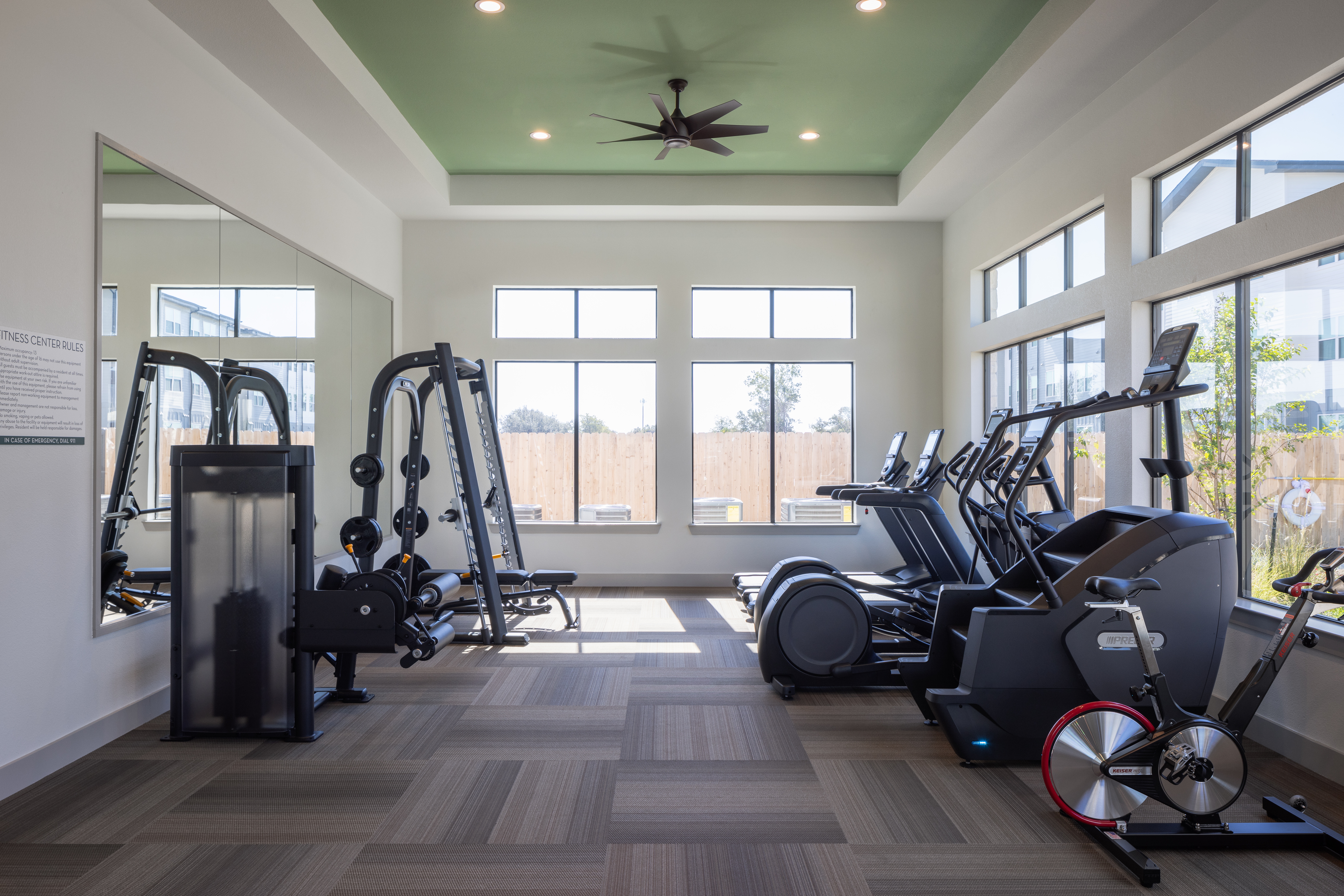 indoor fitness center with free weights, treadmills, bicycle/bike, with large window in the back shining bright light in at prose evergreen apartments in new braunfels, texas