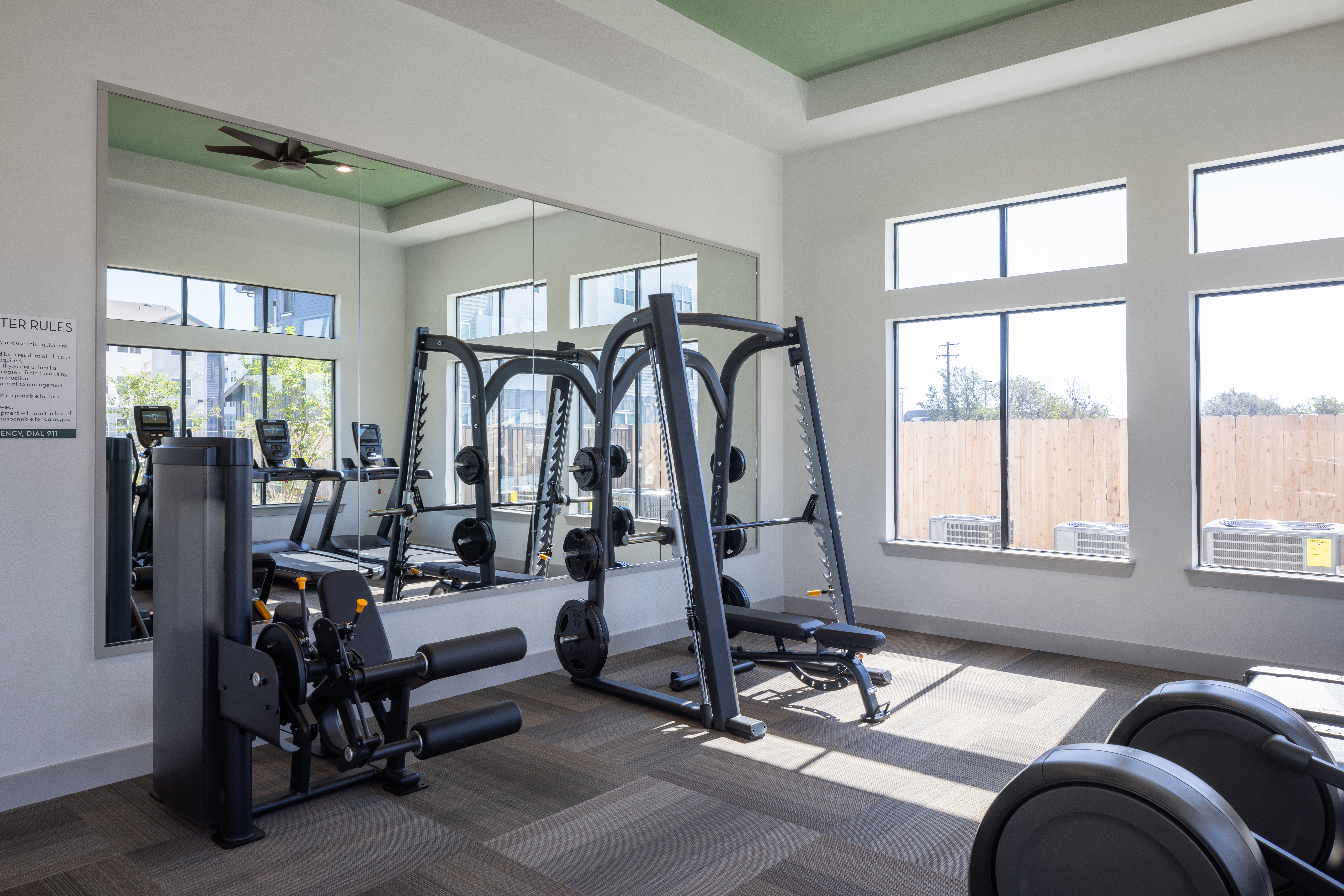 indoor fitness center with free weights, treadmills, bicycle/bike, with large window in the back shining bright light in at prose evergreen apartments in new braunfels, texas