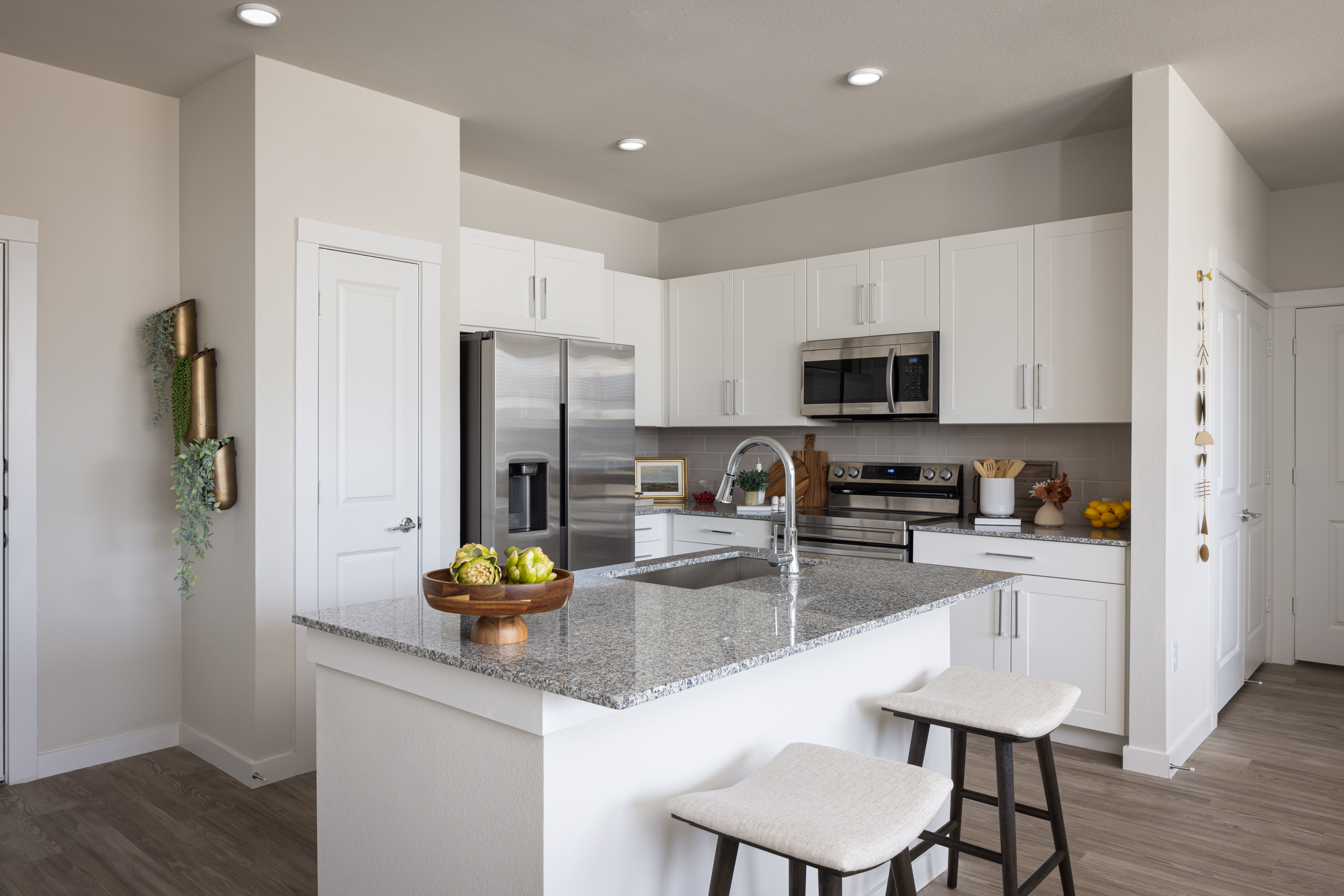 kitchen with white cabinets, grey countertop and chrome faucets with bartstool st the eat in bar at prose evergreen apts in new braunfels, texas